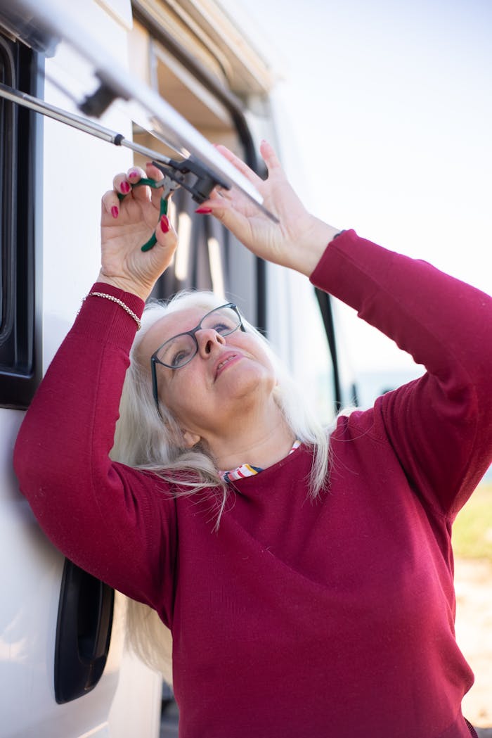 A senior woman concentrates while repairing a camper van outdoors in Portugal.